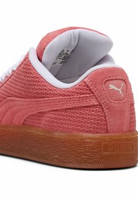 Rozā tekstūrēti sporta apavi ar baltām šņorēm un mīkstu apkakli. Iespējo gumijas zole un mazu zelta Puma logotipu uz papēža.