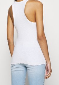 Vit ärmlös tanktopp med rundad halsringning, en något rundad nederkant och en avslappnad passform, tillverkad av mjukt bomullstyg.