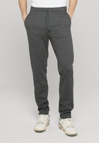 Pantaloni da jogging grigi in tessuto morbido, con vita con coulisse, tasche laterali e gambe affusolate, abbinati a scarpe sportive bianche.