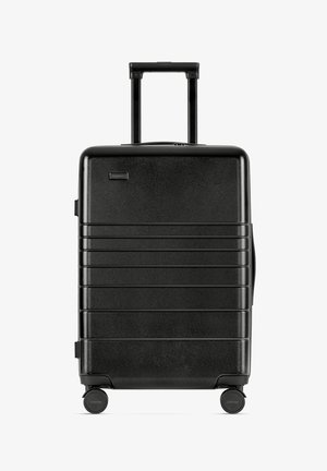 Valigia rigida nera con finitura testurizzata, scanalature verticali, maniglia retrattile e quattro ruote per la mobilità.