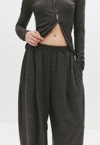 Donkergrijs, textuur langemouwen top met knopen en bijpassende elastische taille, wijde broek. Zichtbare huid op de buik.