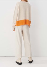 Beżowy sweter z pomarańczowym ściągaczem, w połączeniu z luźnymi beżowymi spodniami i botkami do kostek. Miękka tekstura, casualowy fason.