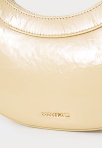 Cream-colored Coccinelle handbag with a smooth, glossy texture, curved shape, and embossed logo; features stitching along the top edge.