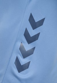 Blauwe stof met vier donkerblauwe chevronpijlen die verticaal in een versprongen patroon langs een naad zijn geplaatst.