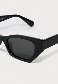 Óculos de sol retangulares pretos com armação grossa e lentes escuras, sobre um fundo branco liso.