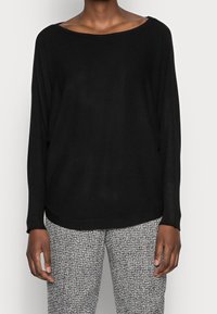 Suéter negro de punto con un escote amplio y mangas largas, combinado con pantalones texturizados de patrón gris y negro. Corte relajado.