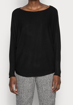 Suéter negro de punto con un escote amplio y mangas largas, combinado con pantalones texturizados de patrón gris y negro. Corte relajado.