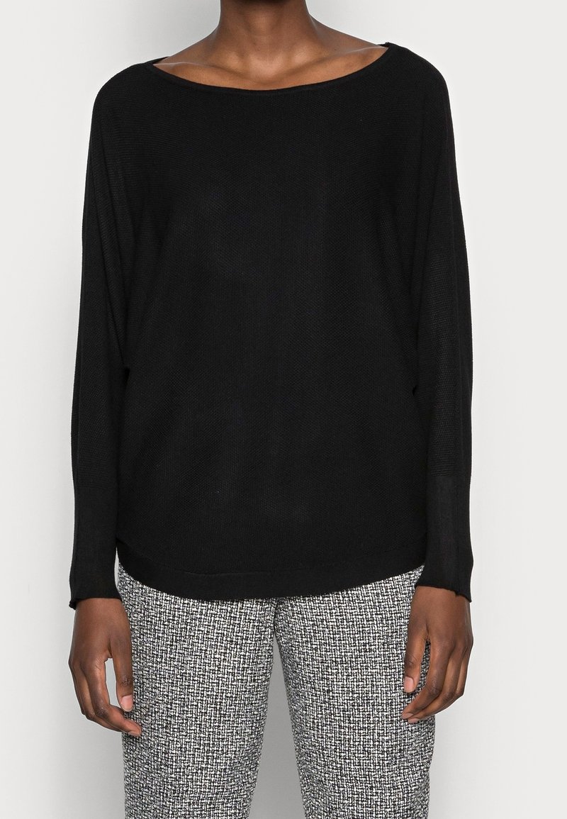 Suéter negro de punto con un escote amplio y mangas largas, combinado con pantalones texturizados de patrón gris y negro. Corte relajado.