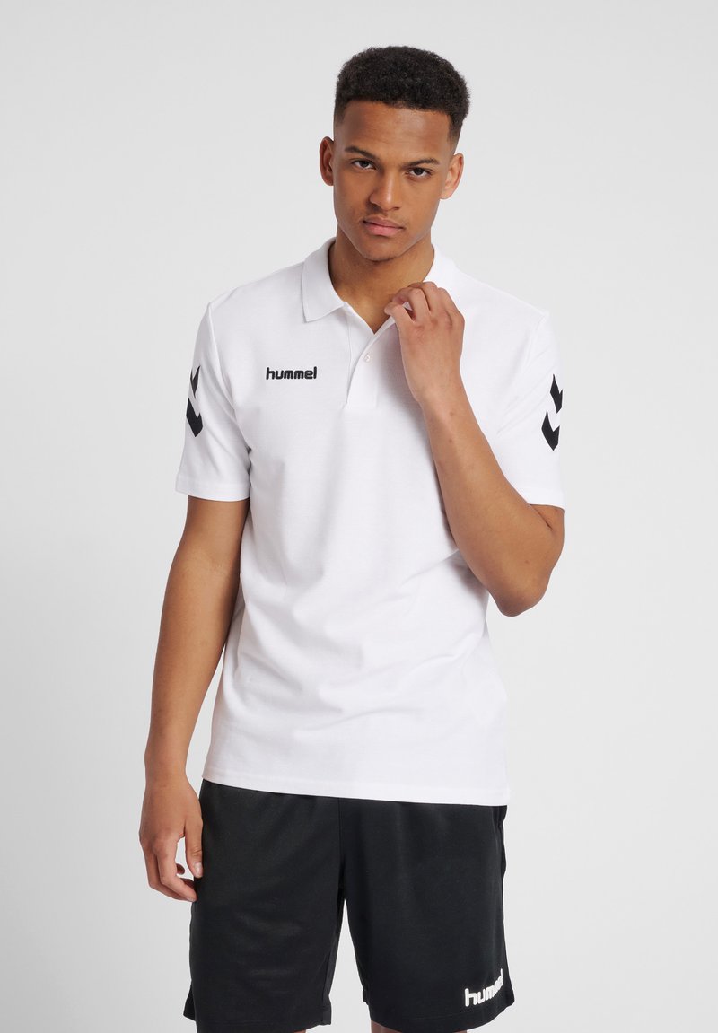 Witte polo shirt gemaakt van katoen met een kraag, voorzien van een zwart hummel logo en zwarte chevronaccenten op de mouwen. Gekozen in combinatie met zwarte shorts.