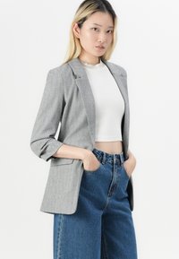 Grijze herringbone blazer met ingesneden revers en opgerolde mouwen, gecombineerd met hooggelegen blauwe denim jeans. Gladde stoftextuur, nauwsluitende pasvorm.