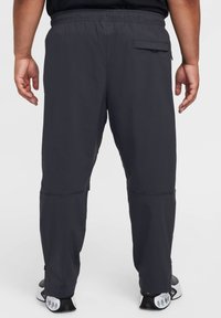 Pantaloni sportivi da uomo in grigio scuro con vestibilità rilassata, elastico in vita e tasca posteriore. Presentano aperture con zip vicino alle caviglie.