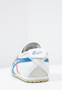 Hvid sneaker med blå og røde striber, ruskindsdetaljer, blød tekstur og et fremtrædende "Tiger"-logo på hælen. Klassisk design.