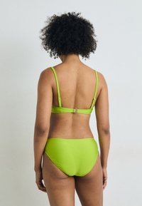 Žalias bikinis su paprastu dizainu. Viršus turi reguliuojamus petnešas, o nugarinė dalis – užsegimą. Audinys atrodo lygus ir blizgus.