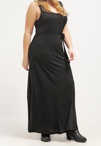 Black maxi dress with a sleeveless design, fitted bodice, cinched waist, and a tie detail, made of smooth, flowing fabric.