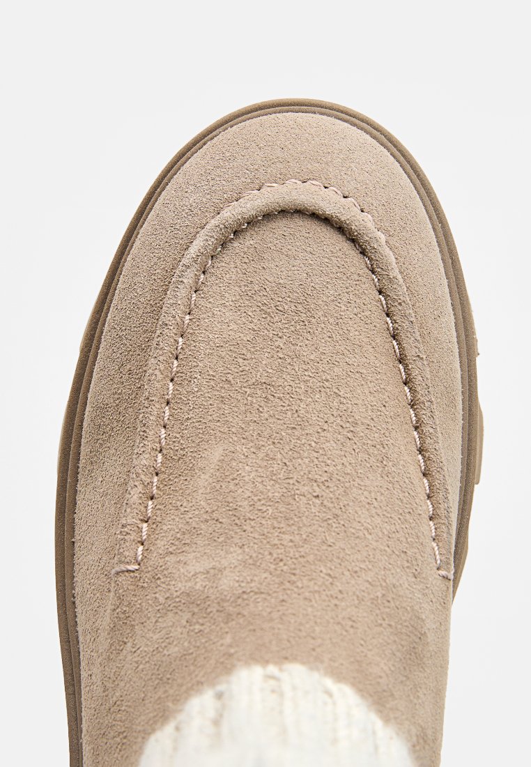 Tannfarbige Wildlederschuhe mit runder Zehenform, genähten Details und strukturiertem Profil, die an der Kante eine gemütliche gestrickte Socke zeigen.