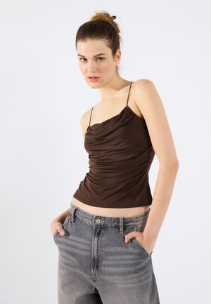 T-shirt brun drapé avec de fines bretelles, associé à un jean gris délavé taille haute avec des poches avant et de subtiles rayures verticales.