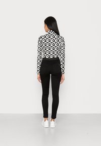 Jeans pretos ajustados com uma cintura alta, combinados com uma blusa de mangas longas em padrão preto e branco com formas geométricas. Ténis brancos em destaque.