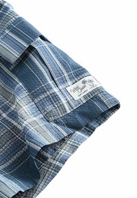 Camicia a maniche corte a quadri blu in tessuto testurizzato con strisce variate; presenta un'etichetta con la scritta "West Coast Surf Supply."