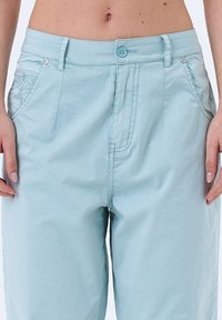 Lichtblauwe broek van een gladde, lichte stof, met een rechte taille en subtiele borduursels op de zakken, met een knoopsluiting.