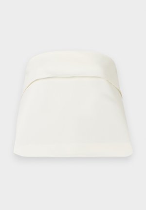 Lit queen-size avec une couette douce de couleur crème et un grand oreiller plié, placé devant un fond clair uni.