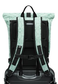 Zaino verde a motivi con design a risvolto, dotato di spallacci neri regolabili e imbottitura in rete sul retro, attaccato a una valigia nera.