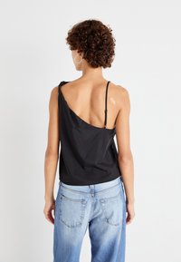 Haut asymétrique noir avec une fine bretelle et un drapé en tissu, associé à un jean en denim bleu clair. Texture lisse et design décontracté.