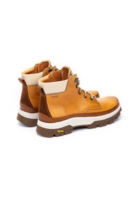 Botas de cuero marrón hasta el tobillo con un acabado texturizado, cuello blanco, ojales metálicos y suela Vibram para mayor tracción.