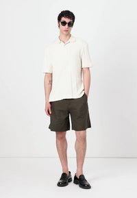 Kremfarvet ribbet polo skjorte, olivengrønne shorts og sorte loafers. Solbriller tilføjer et moderne præg. Minimalistisk design med rene linjer.