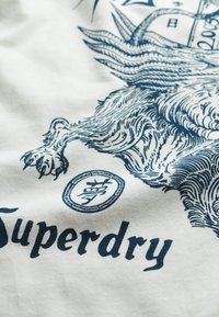 Witte katoenen t-shirt met een donkerblauwe afbeelding van een leeuw en het logo "Superdry" in vette letters, met intrigerende details en texturen.