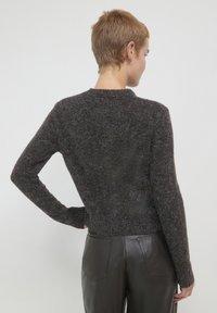 Brauner, strukturierten Pullover mit langen Ärmeln und rundem Ausschnitt, cropped Schnitt, getragen mit eleganten schwarzen Lederhosen.