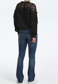 Sweatshirt noir avec des détails en dentelle aux épaules, associé à un jean flare en denim bleu ajusté et des baskets blanches.