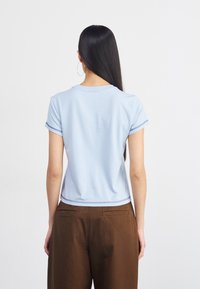 T-shirt azul claro de manga curta com punhos enrolados, decote redondo e uma bainha mais curta, combinado com calças largas castanhas.