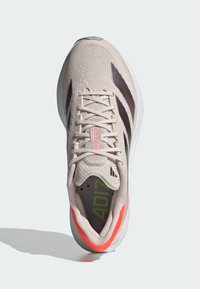 Béžová a hnědá běžecká bota Adidas s růžovým nápisem "ADIZERO" na jazyku, oranžovým akcentem na patě a bílou podrážkou, pohled zespodu.