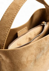 Borsa in suede color beige chiaro con interno in pelle liscia. Presenta un compartimento con zip, forma strutturata e manico arrotondato.