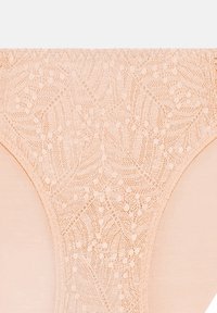 Biancheria intima in pizzo di un morbido colore pesca, caratterizzata da un delicato motivo a foglia e bordi lisci e senza cuciture per comfort e vestibilità.
