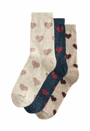 Three pairs of socks in mixed materials. One beige with light brown hearts, one dark blue with red hearts, and one beige with dark brown hearts.