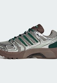 Sport shoe with a mesh upper in silver and green, featuring metallic accents and a thick brown sole. Designed for comfort and breathability.