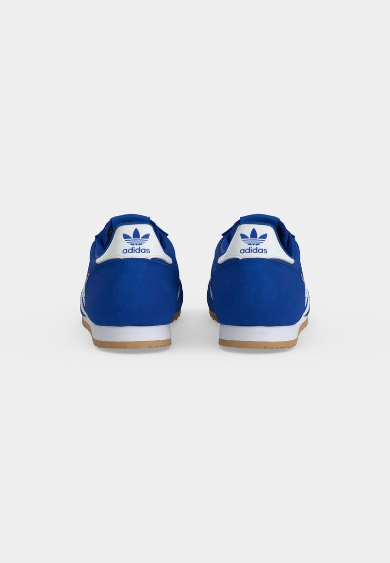 Een paar blauwe Adidas sneakers gezien van achteren, met witte hielstukjes met blauwe Adidas trefoil-logo's en zool in gumkleur.