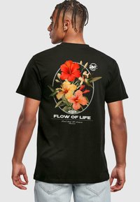 Black cotton t-shirt featuring a floral design with red and orange hibiscus, hummingbirds, and the text "FLOW OF LIFE" in white.