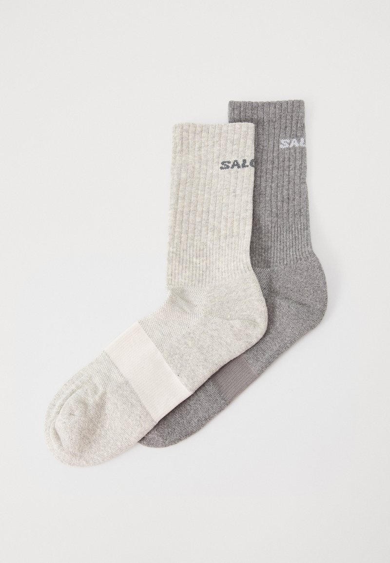 Dos pares de calcetines acanalados: uno de color gris claro con una banda blanca, el otro de color gris oscuro con "SAL" impreso en blanco. Ambos tienen una textura suave.