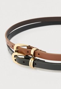 Two slim leather belts, one brown and one black, with gold metal buckles and loops, coiled on a plain white surface.