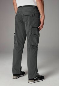 Grå cargo-bukser har flere lommer, en lynlåslomme på siden og en slim fit. Bæres med sorte sneakers og en neutral skjorte.