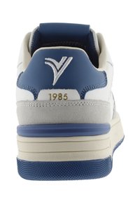Zapatillas de hombre con cuero blanco y gamuza gris, acentos azules, cuello acolchado, logo elevado y el año "1985" en dorado en el talón.