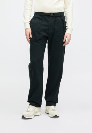 Pantalons cargo noirs à coupe décontractée, dotés d'une ceinture, de poches latérales et d'un tissu en mélange de coton. Portés avec des chaussures de sport de couleur claire.