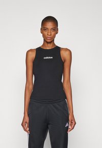 Juodas prigludęs marškinėliai be rankovių su apvalia iškirpte, ant krūtinės puikuojasi balta Adidas logotipas. Pora juodų elastinių kelnių su juosmeniu, subtilus ženklas.