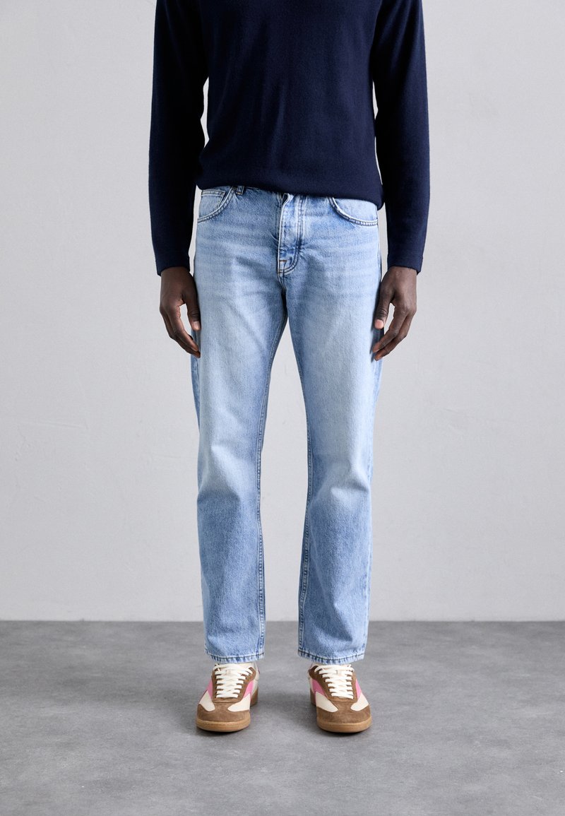 Lys blå denim jeans med rett snitt, parret med kremfargede og brune sneakers med rosa detaljer, iført en marineblå langermet skjorte.