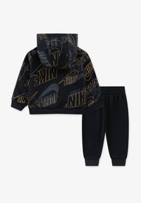 Temš zilas krāsas kapucīna krekls un atbilstošas sporta bikses, izgatavotas no mīkstas auduma. Kapucīnam ir kapuce, un tajā ir zelta toņu prints ar tekstu "NIKE JUST DO IT".