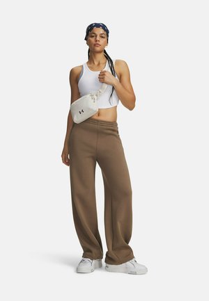 Vrouw draagt een wit cropped topje, bruine wijde broek, witte sneakers, een zwarte bandana en een kleine witte crossbody tas, staand op een witte achtergrond.
