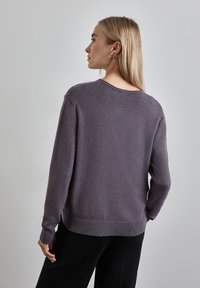 Violetti neulepaita, jossa on rento leikkaus, pyöreä pääntie, ribbikuvioidut hihansuut ja helma. Omistaa pehmeän tekstuurin ja näyttää kevyeltä.
