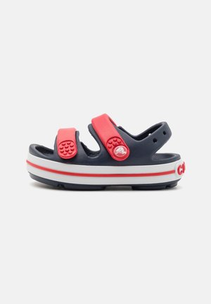 Sandale pour enfants bleu marine et rouge à bout ouvert avec des brides réglables et une semelle blanche avec une bande rouge.